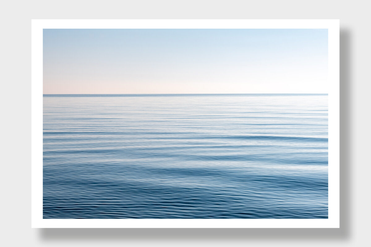 A serene image of the Aegean Sea, Greek coast, with calm waters, mirror-like sea, and a blue sky.