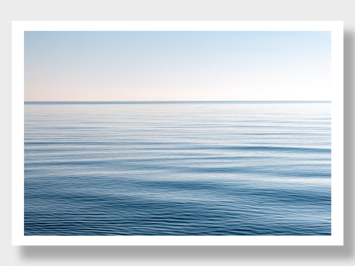 A serene image of the Aegean Sea, Greek coast, with calm waters, mirror-like sea, and a blue sky.