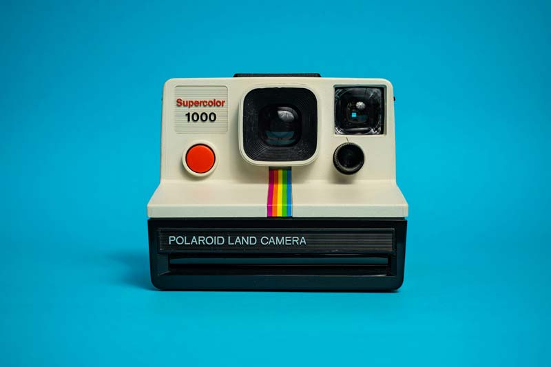 Vintage Polaroid Land Camera with rainbow stripe on blue background